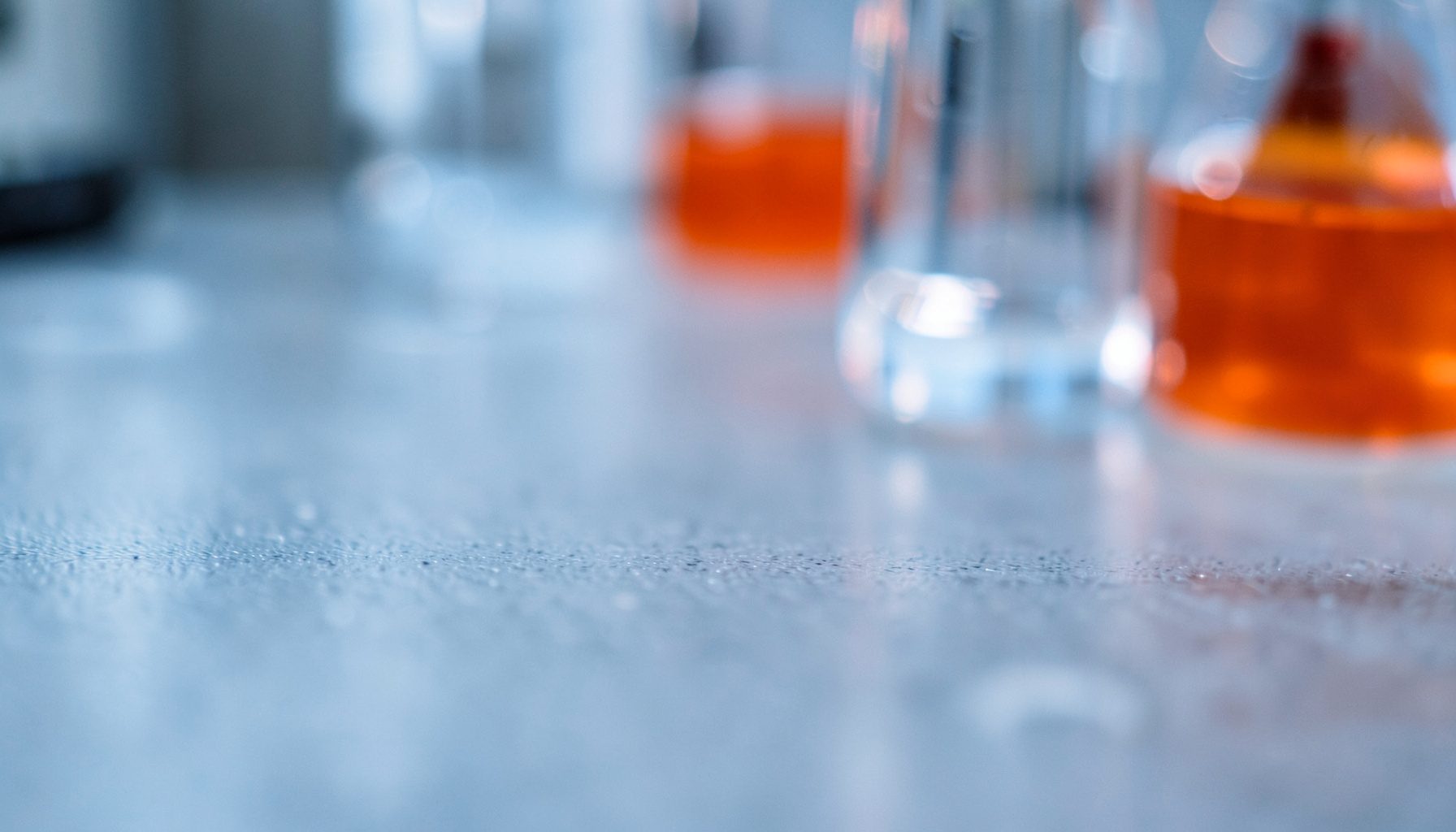 Extreme close-up photograph of a laboratory bench surface in soft focus, cool blue-grey tones with subtle reflections