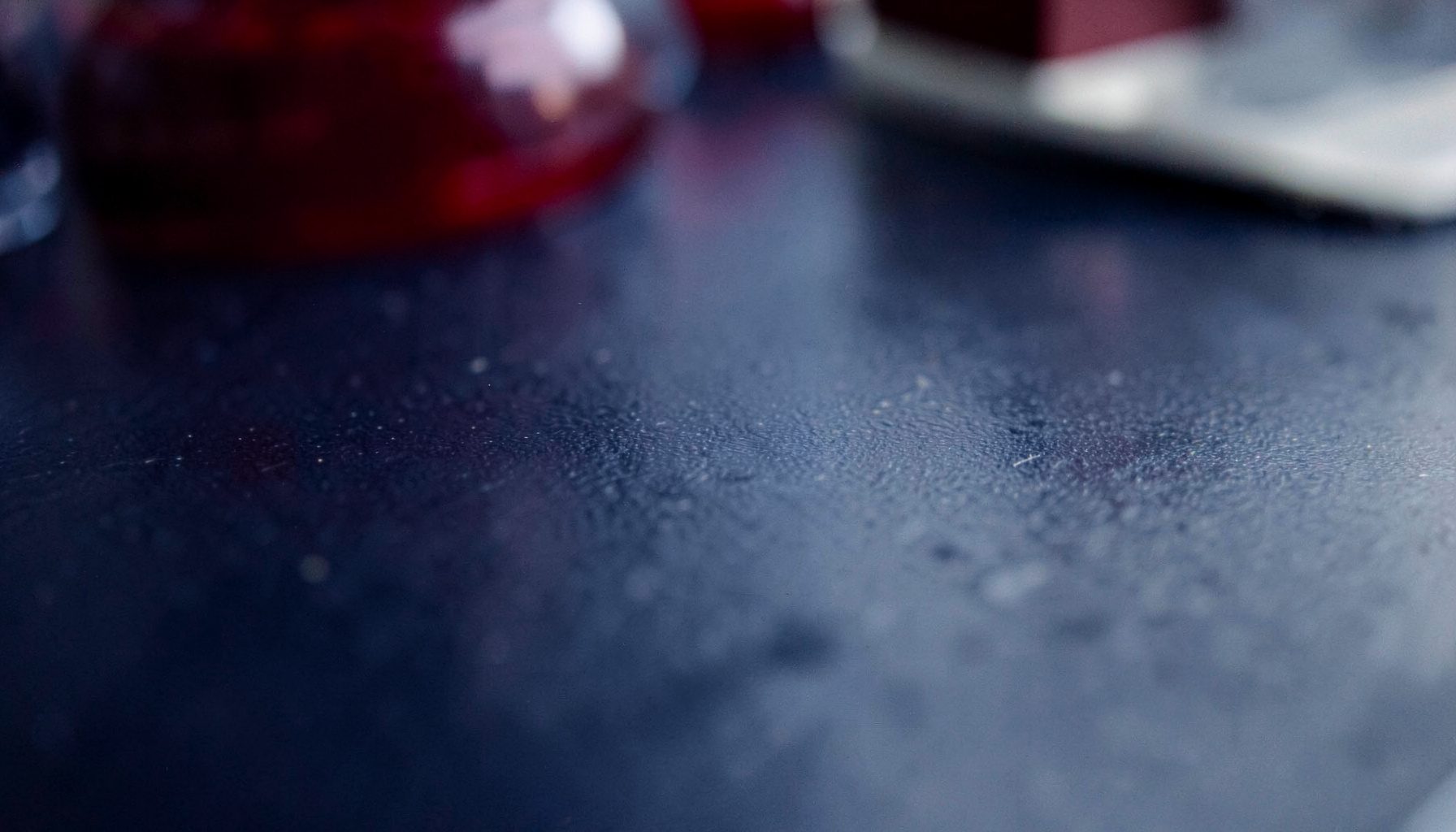 Abstract close-up of a laboratory bench surface in deep navy and steel grey tones, with subtle reflections